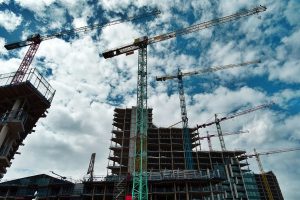 Urban construction site with numerous cranes framing rising skyscrapers against a blue sky.